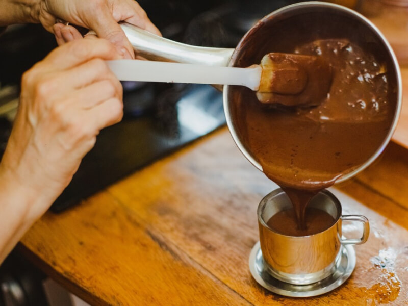 Close up of someone pouring melted chocolate into a metal cup